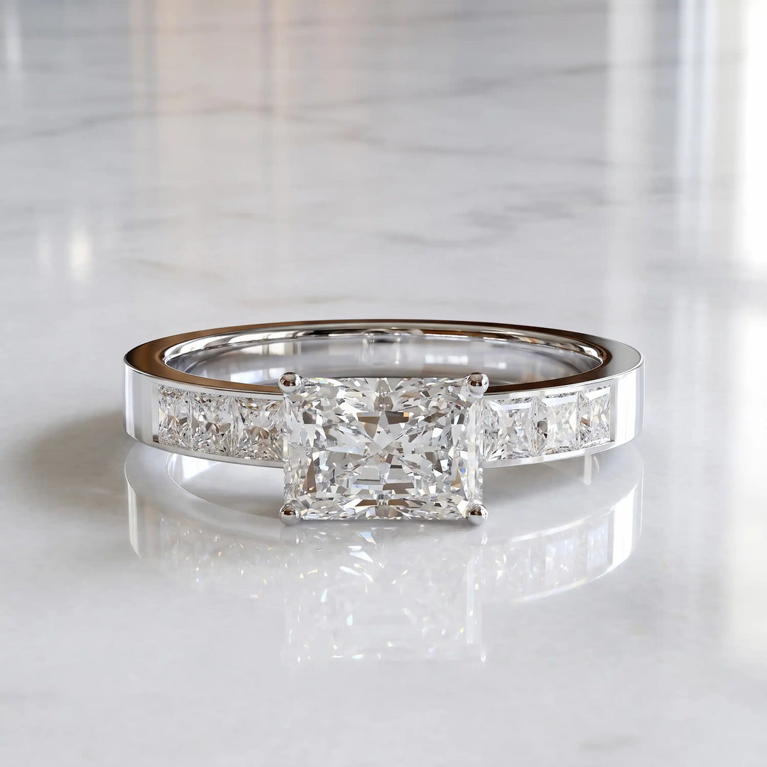 Radiant lab-grown diamond east-west engagement ring with channel-set princess side stones displayed on surface.