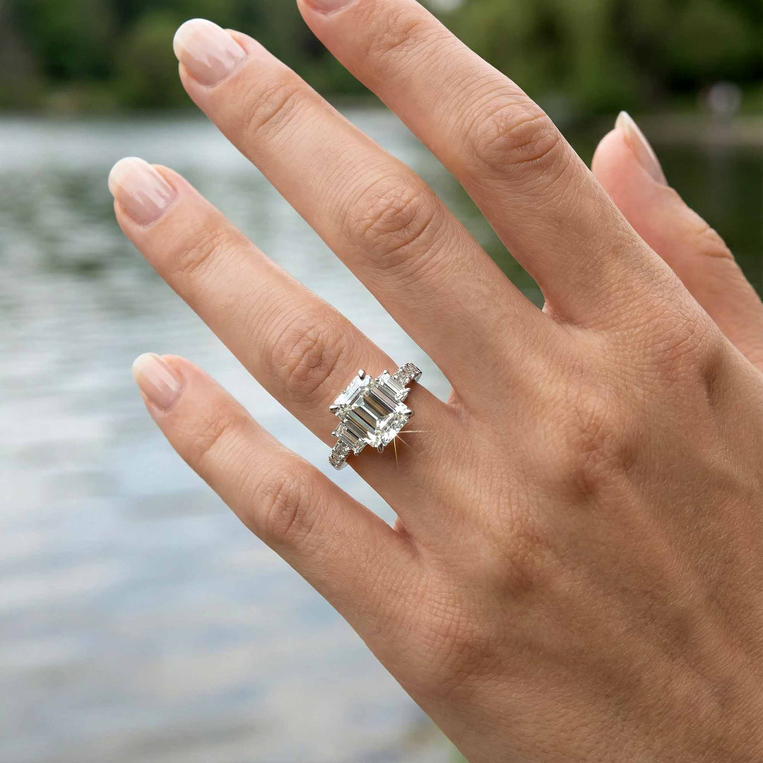 Emerald cut three stone diamond engagement ring with pavé band on display.
