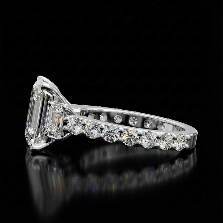 Emerald cut three stone diamond engagement ring with pavé band on display.
