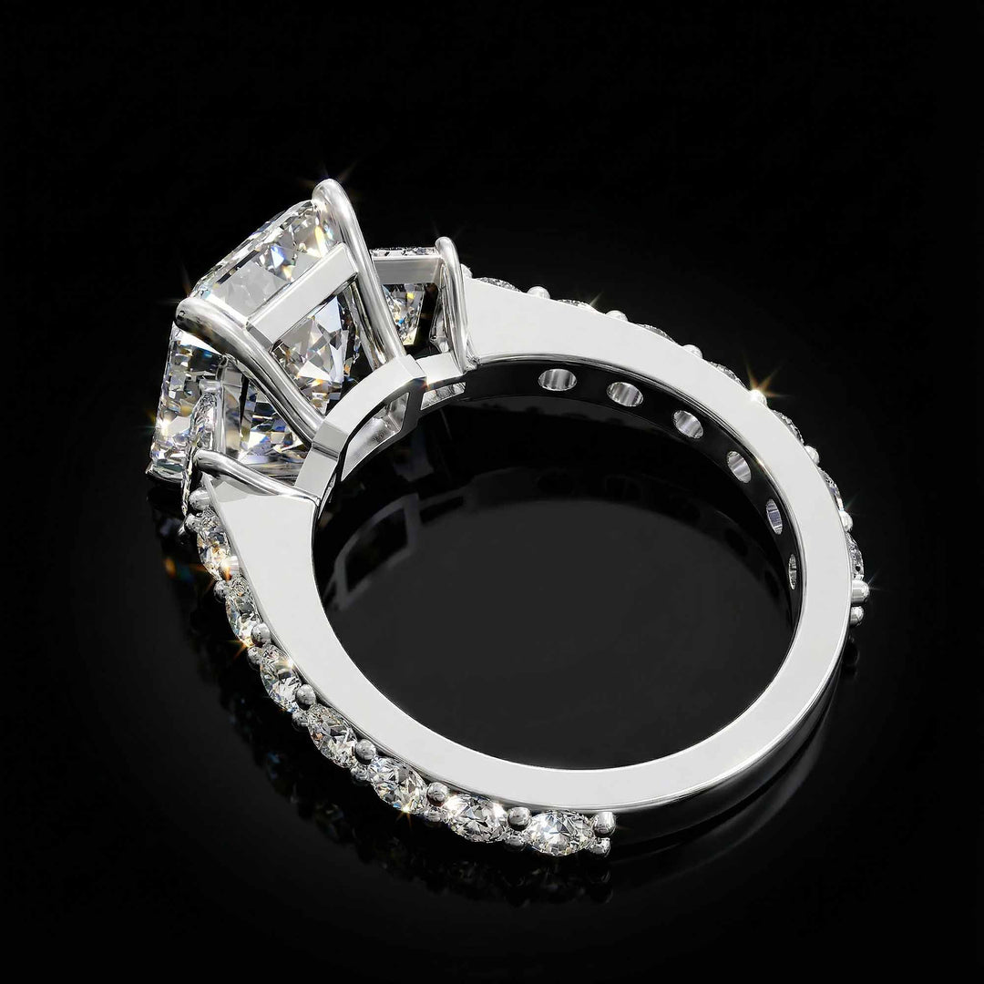 Emerald cut three stone diamond engagement ring with pavé band on display.