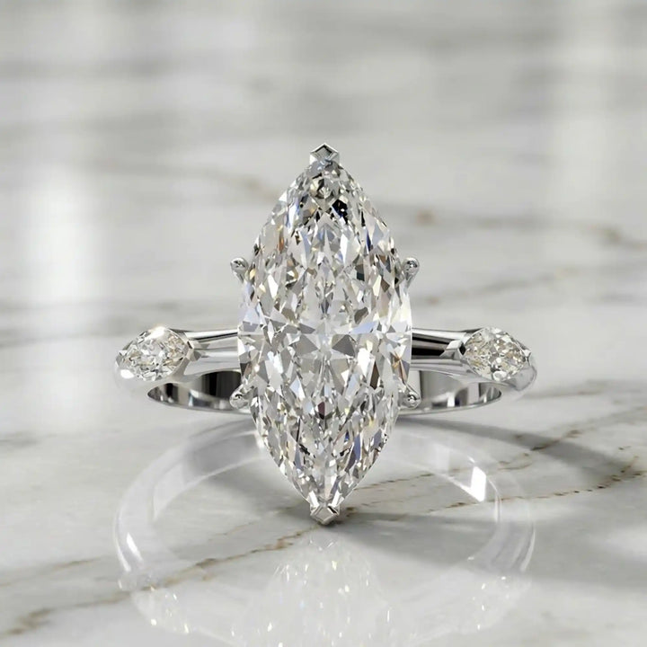 Marquise lab-grown diamond three-stone engagement ring with hidden halo shown on marble display.