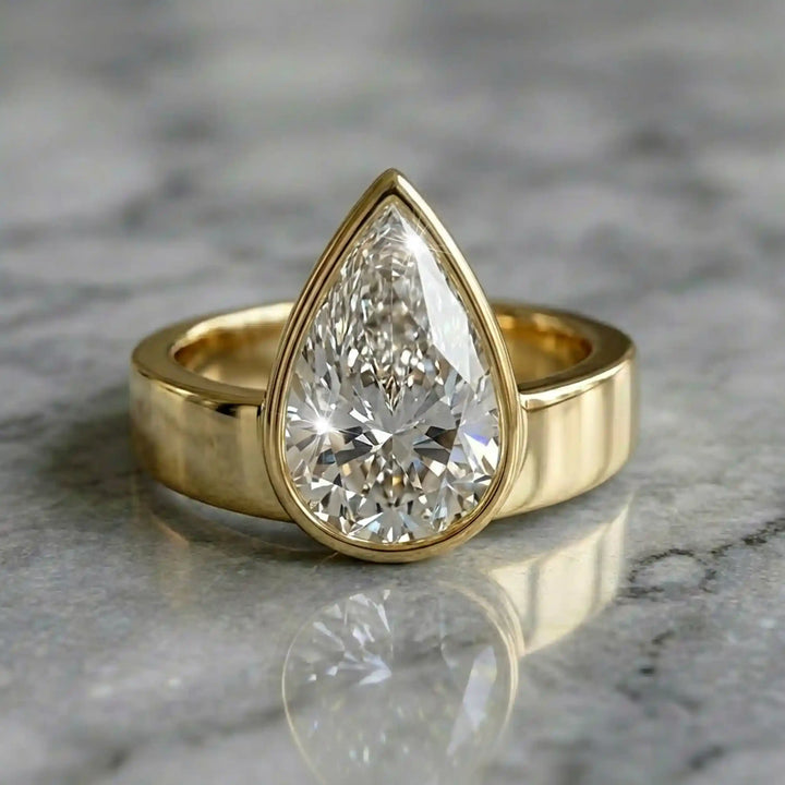 3 carat pear-shaped lab-grown diamond bezel solitaire engagement ring displayed on marble surface.
