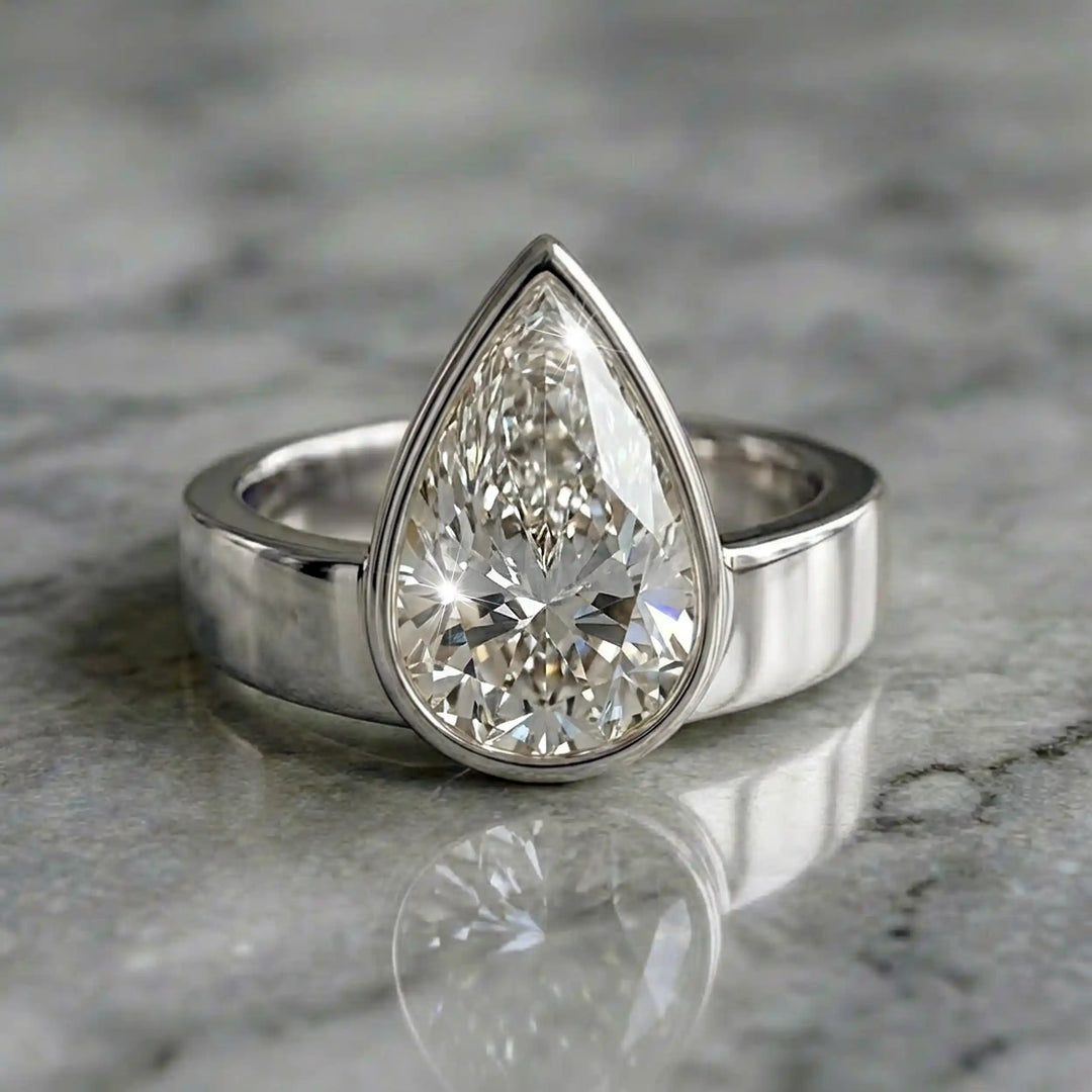 3 carat pear-shaped lab-grown diamond bezel solitaire engagement ring displayed on marble surface.
