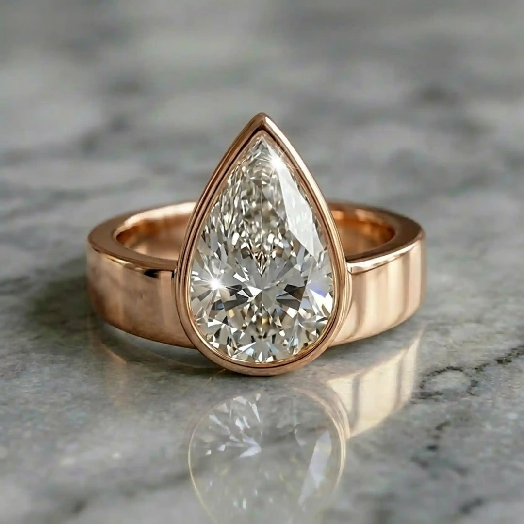 3 carat pear-shaped lab-grown diamond bezel solitaire engagement ring displayed on marble surface.
