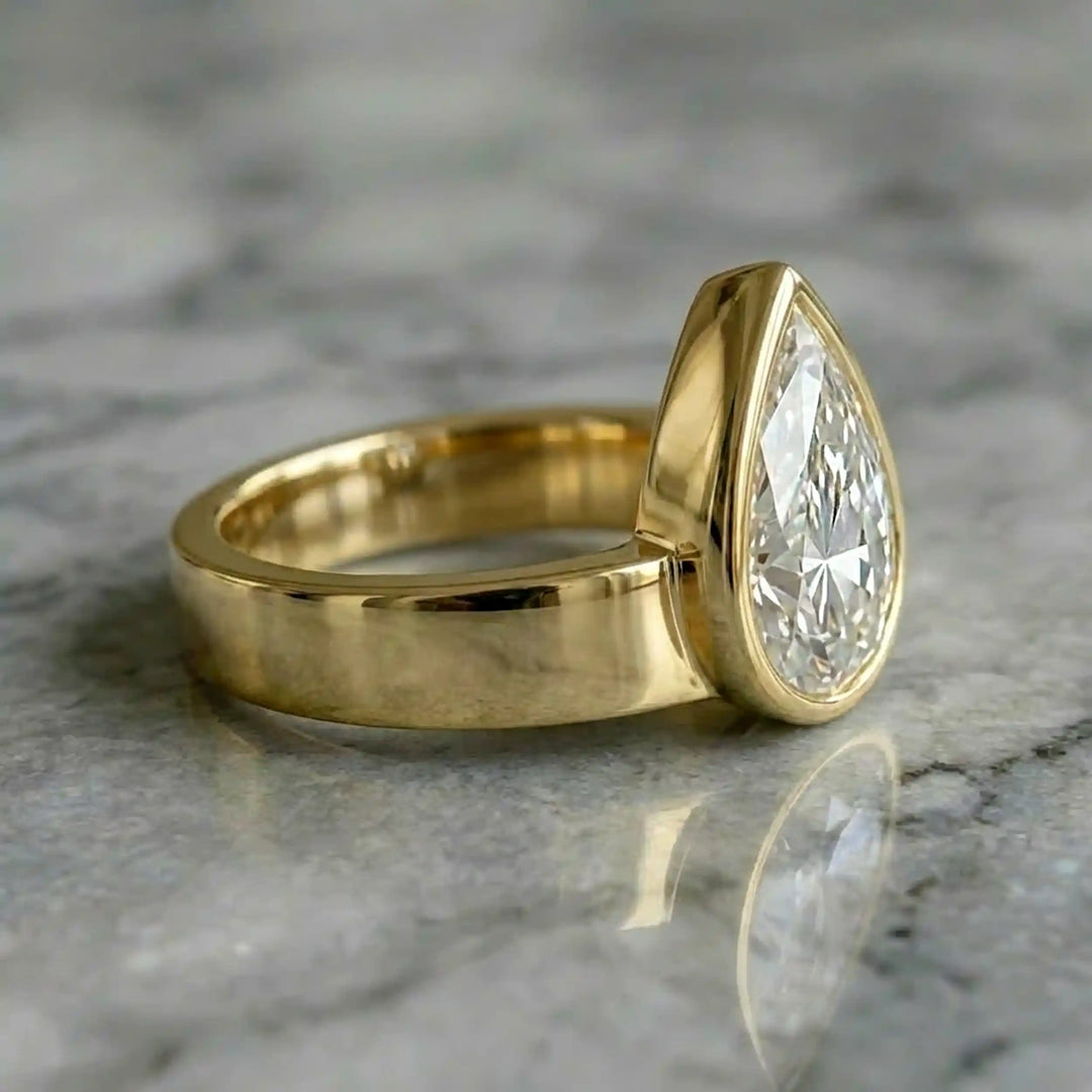 3 carat pear-shaped lab-grown diamond bezel solitaire engagement ring displayed on marble surface.
