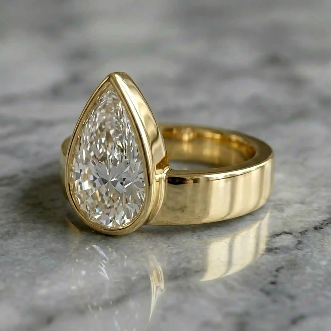3 carat pear-shaped lab-grown diamond bezel solitaire engagement ring displayed on marble surface.
