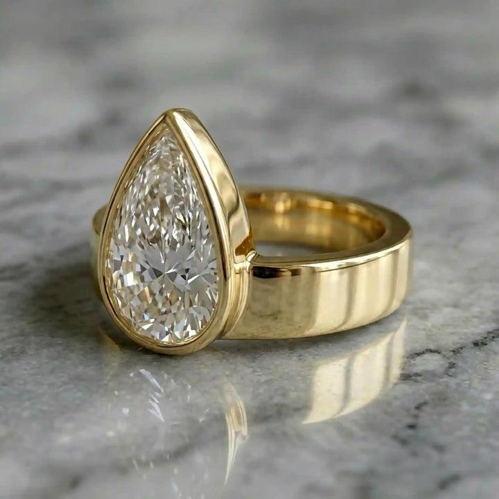 3 carat pear-shaped lab-grown diamond bezel solitaire engagement ring displayed on marble surface.
