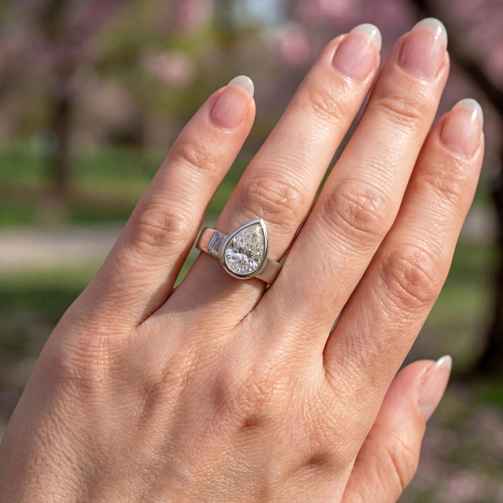 3 carat pear-shaped lab-grown diamond bezel solitaire engagement ring displayed on hand.
