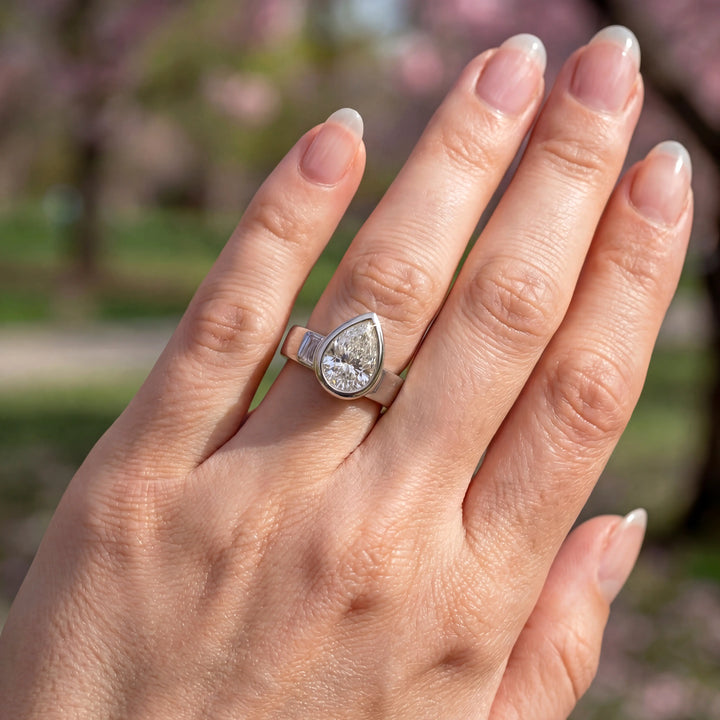 3 carat pear-shaped lab-grown diamond bezel solitaire engagement ring displayed on hand.
