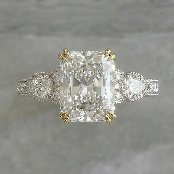 Radiant lab-grown diamond engagement ring with pear side stones displayed on ring stand.
