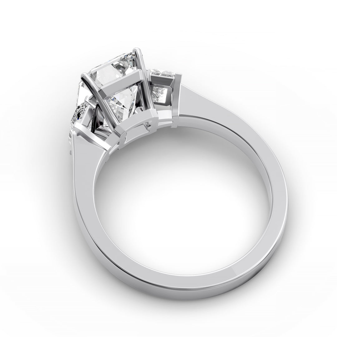 Emerald-cut three-stone diamond engagement ring with matching emerald side stones shown in studio lighting.