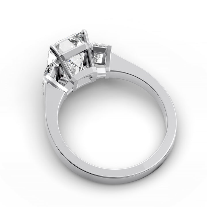 Emerald-cut three-stone diamond engagement ring with matching emerald side stones shown in studio lighting.