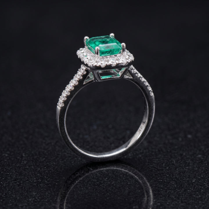 Colombian emerald ring with diamond halo and split shank in 14k white gold.