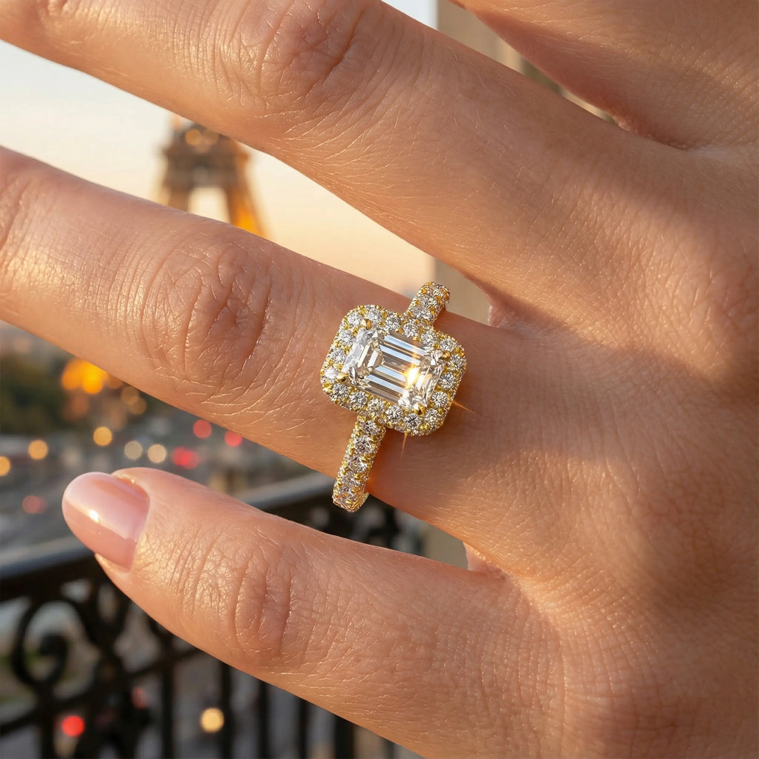 Emerald-cut diamond halo engagement ring with triple prong-set diamond band shown in display view.