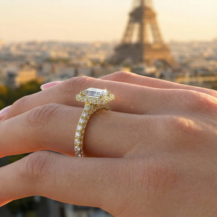 Emerald-cut diamond halo engagement ring with triple prong-set diamond band shown in display view.