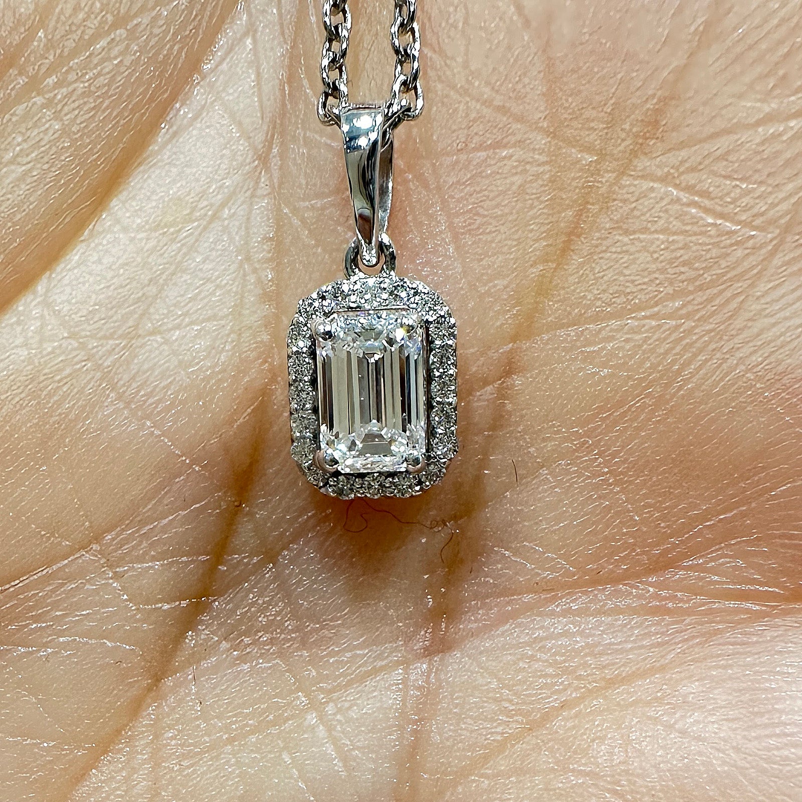 Close-up of a 10K white gold pendant featuring a 0.50ct emerald-cut lab diamond with a halo of smaller diamonds.