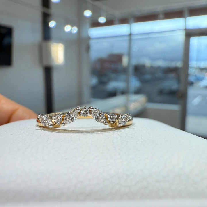 Close-up of a lab-grown marquise and round diamond curved wedding band with shared prongs in a bright showroom setting.