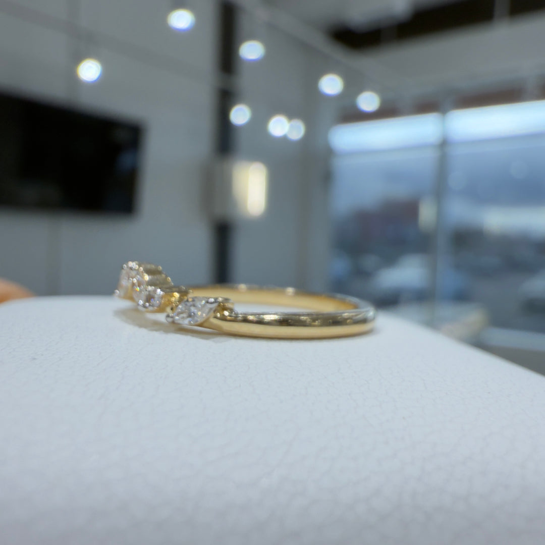 Close-up of a lab-grown marquise and round diamond curved wedding band with shared prongs in a bright showroom setting.