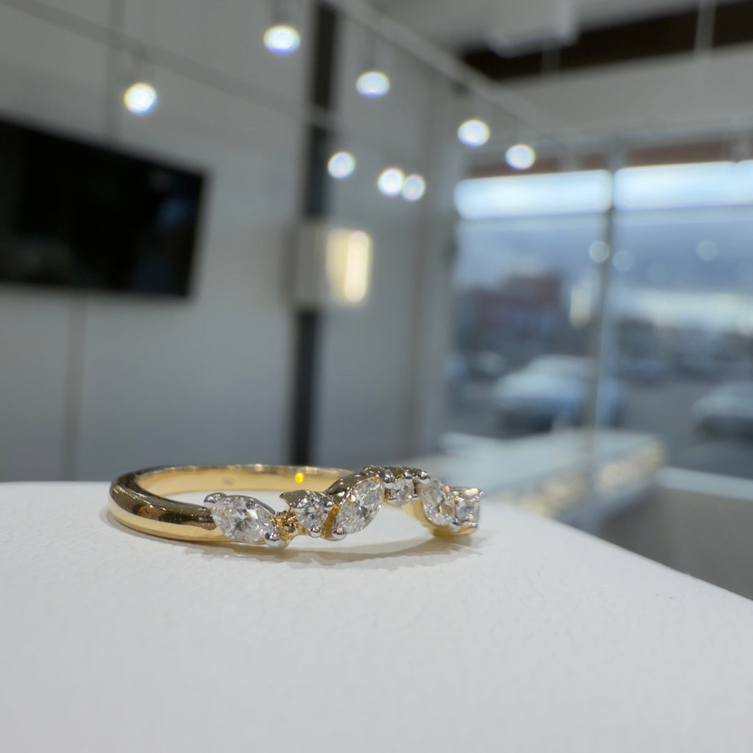 Close-up of a lab-grown marquise and round diamond curved wedding band with shared prongs in a bright showroom setting.