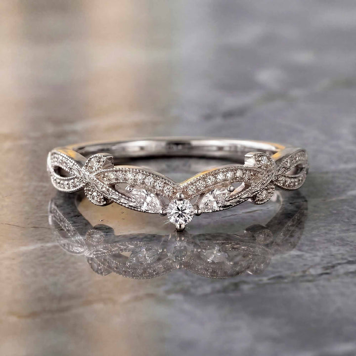Curved wedding band with marquise and round lab-grown diamonds shown on reflective surface.