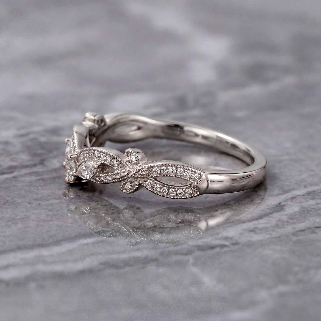 Curved wedding band with marquise and round lab-grown diamonds shown on reflective surface.