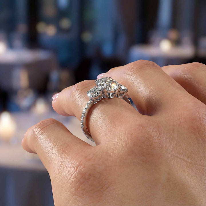 Oval diamond three stone engagement ring with round side stones and pavé band on display.
