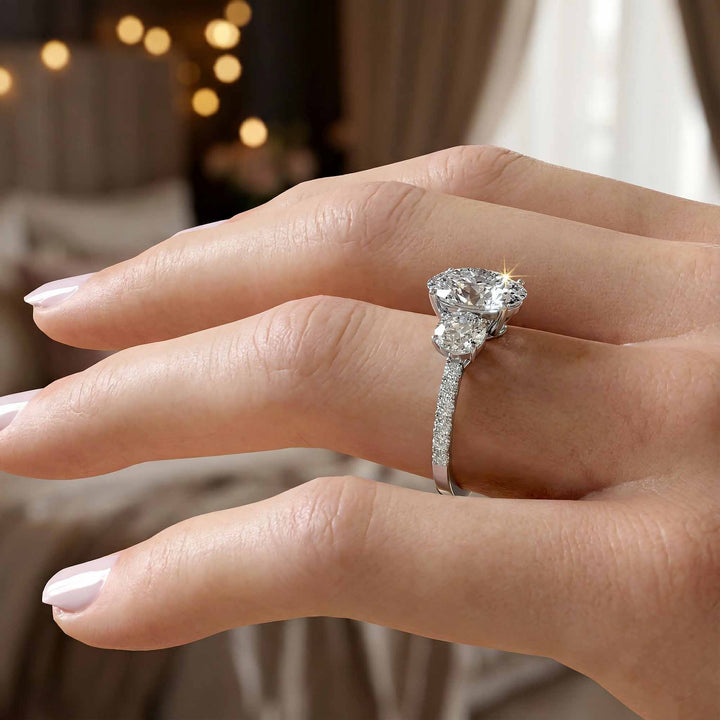 Oval diamond three stone engagement ring with round side stones and pavé band on display.
