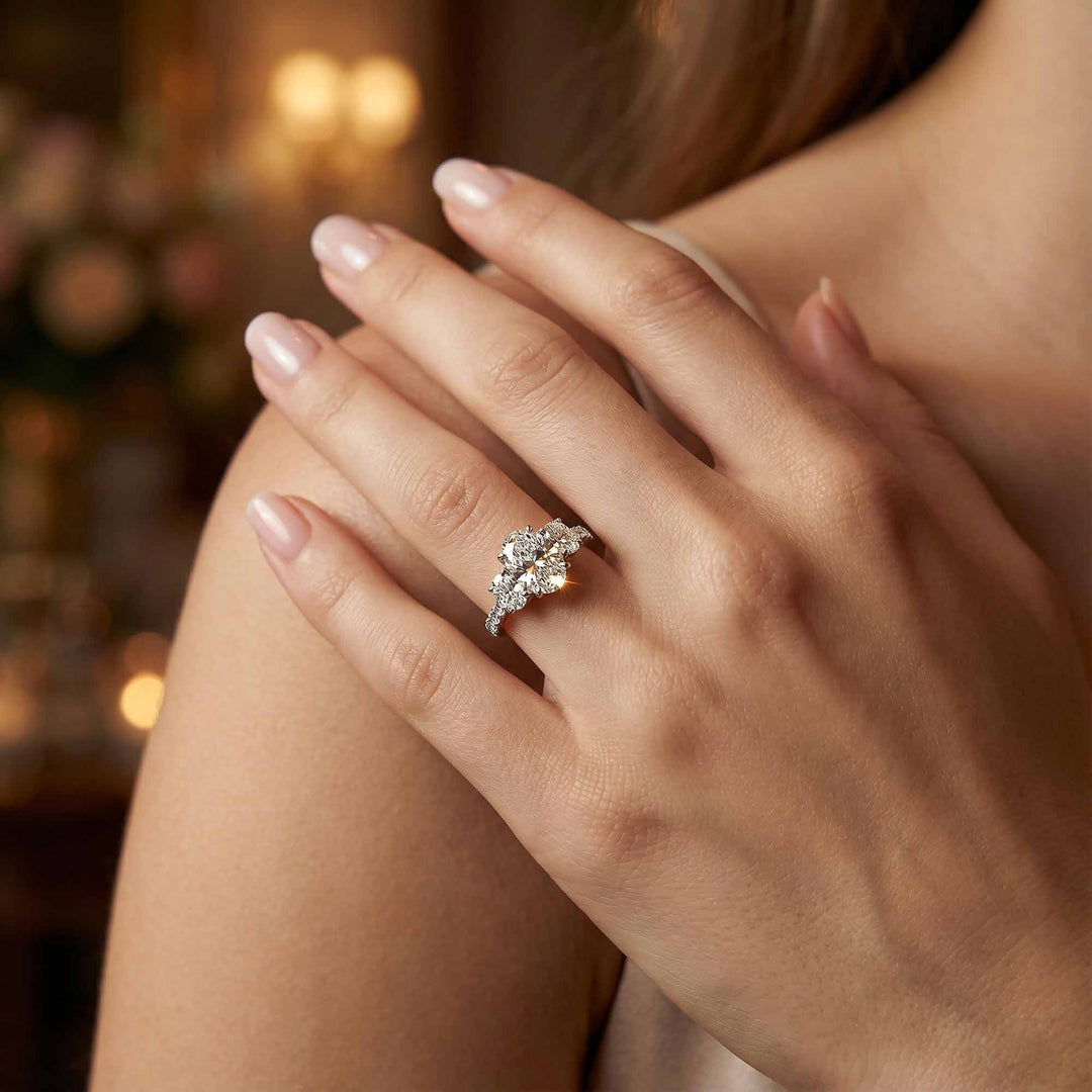 Oval diamond three stone engagement ring with round side stones and pavé band on display.

