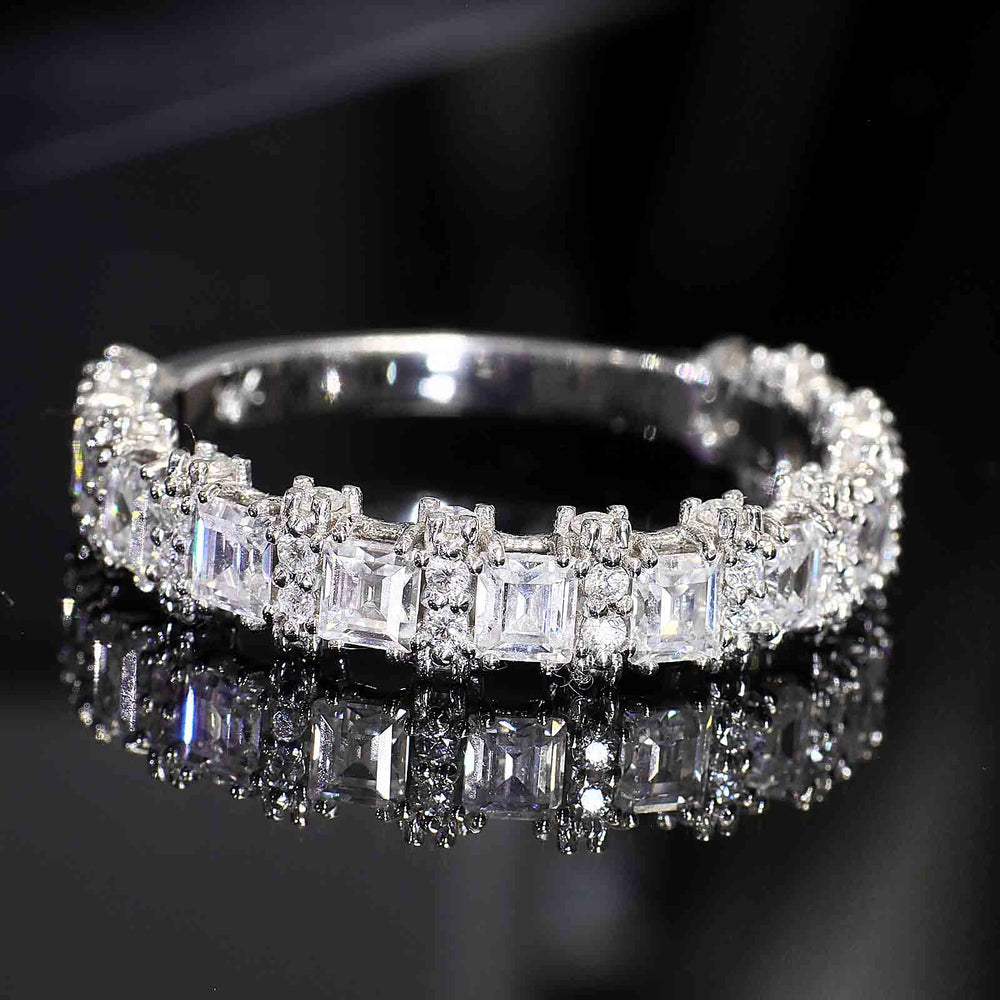 A diamond band with princess-cut and round diamonds featuring half-halo accents and a tapered V-shaped bottom design, displayed on a reflective surface.