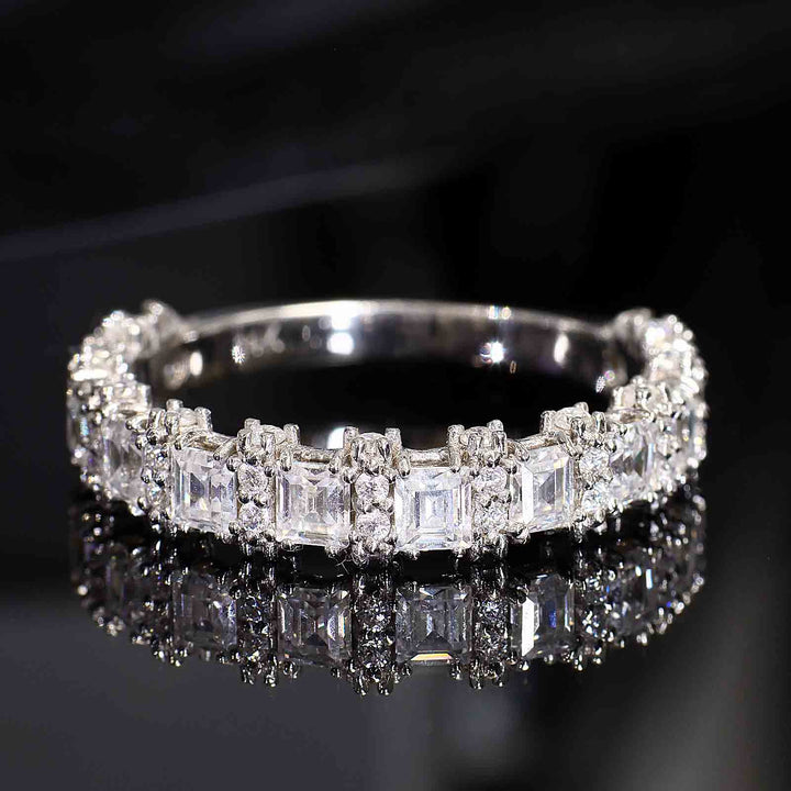 A diamond band with princess-cut and round diamonds featuring half-halo accents and a tapered V-shaped bottom design, displayed on a reflective surface.