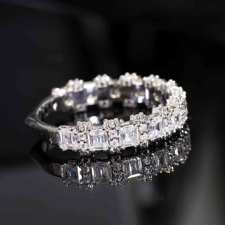 A diamond band with princess-cut and round diamonds featuring half-halo accents and a tapered V-shaped bottom design, displayed on a reflective surface.