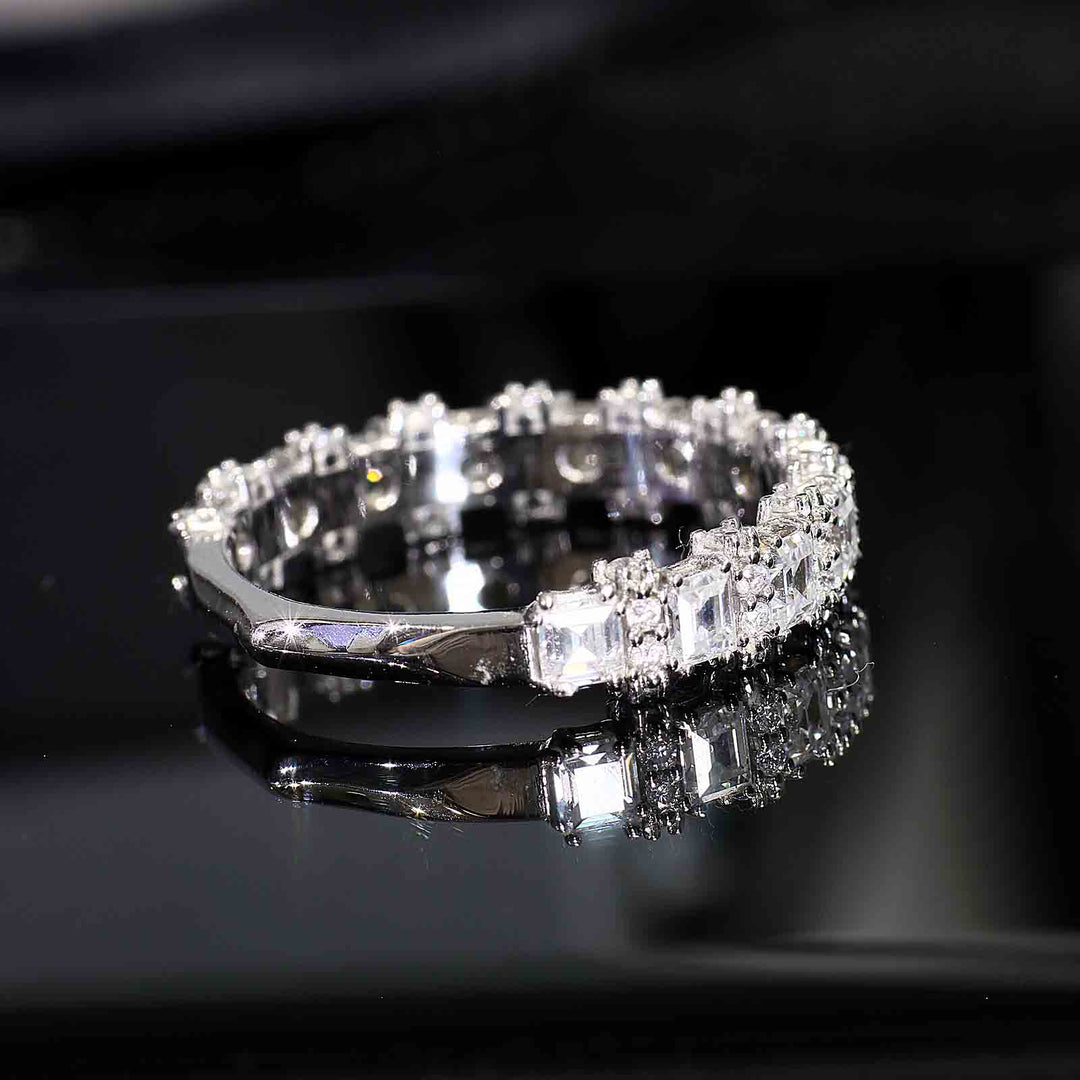 A diamond band with princess-cut and round diamonds featuring half-halo accents and a tapered V-shaped bottom design, displayed on a reflective surface.