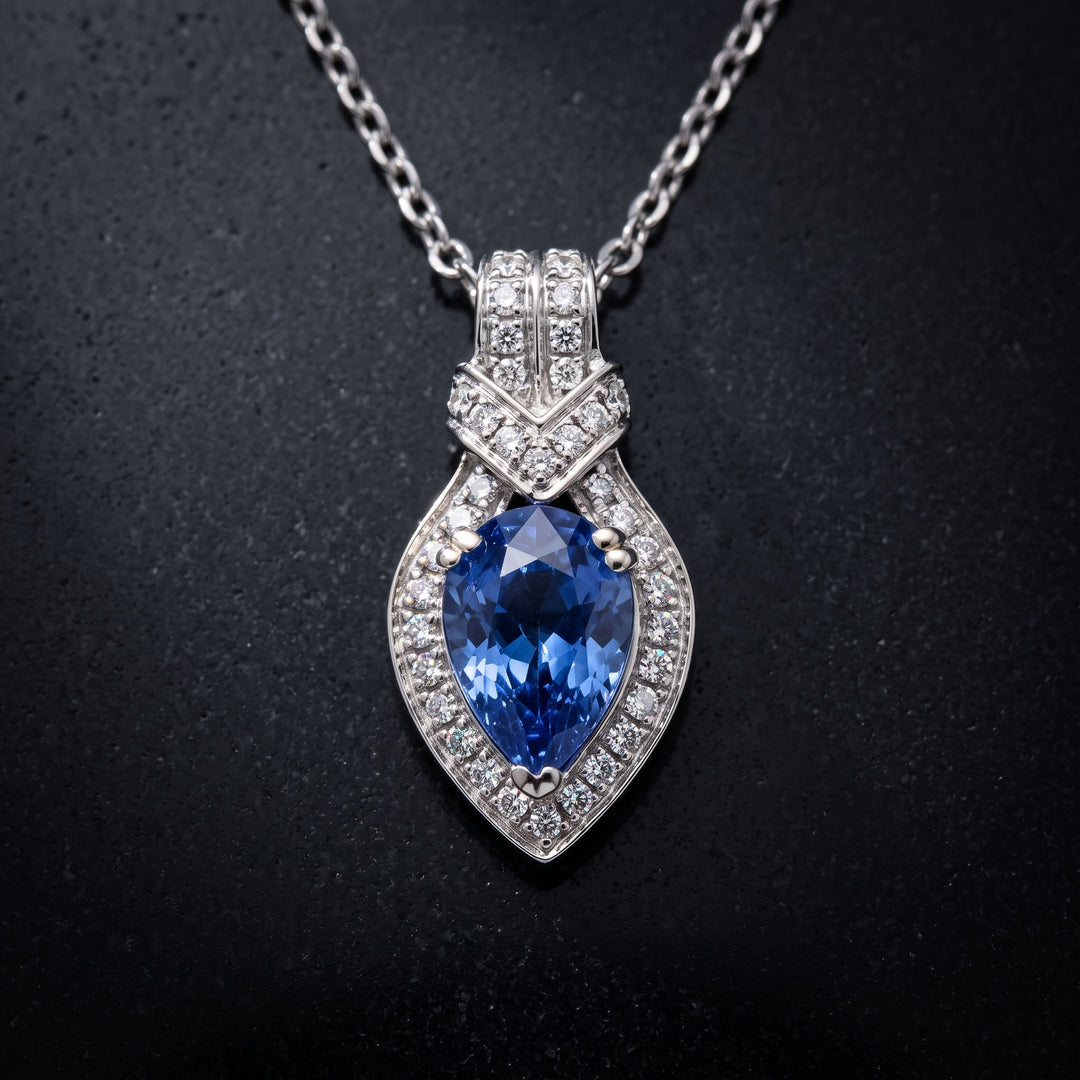 Pear-cut blue sapphire pendant with diamond halo in 14K white gold.