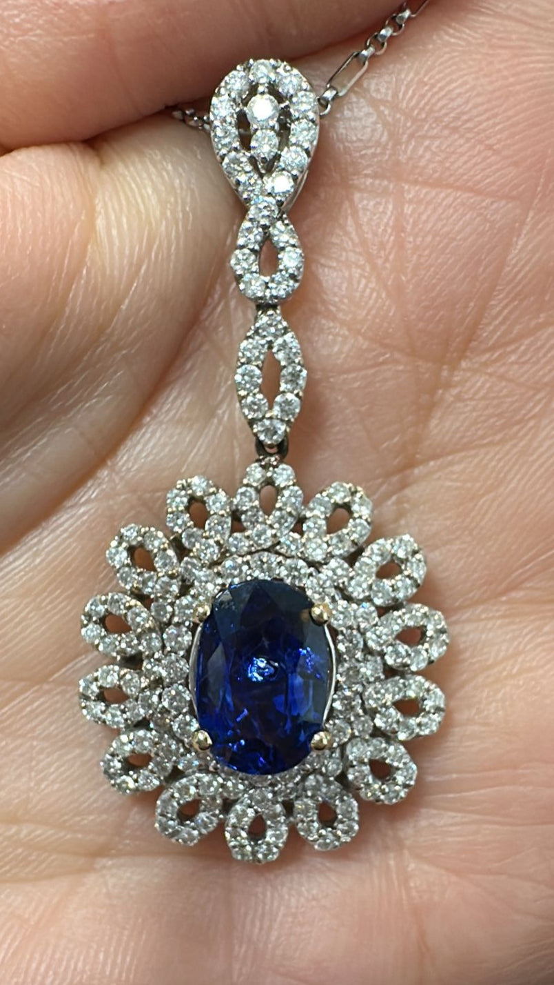 Oval-cut blue sapphire pendant with ornate diamond halo in 18K white gold.