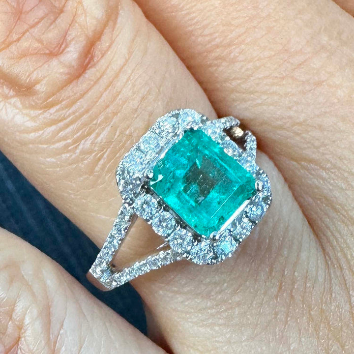 Colombian emerald ring with diamond halo and split shank in 14k white gold.