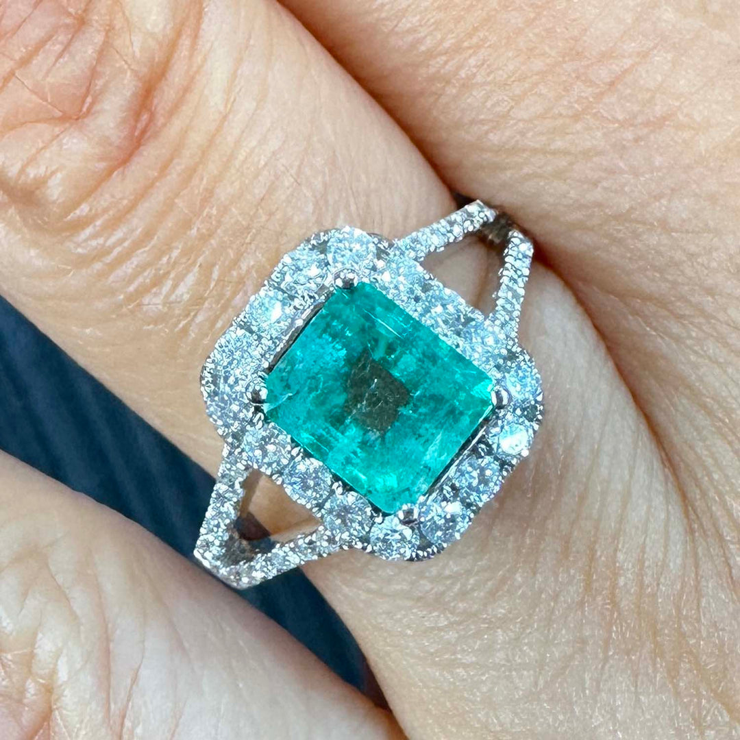 Colombian emerald ring with diamond halo and split shank in 14k white gold.