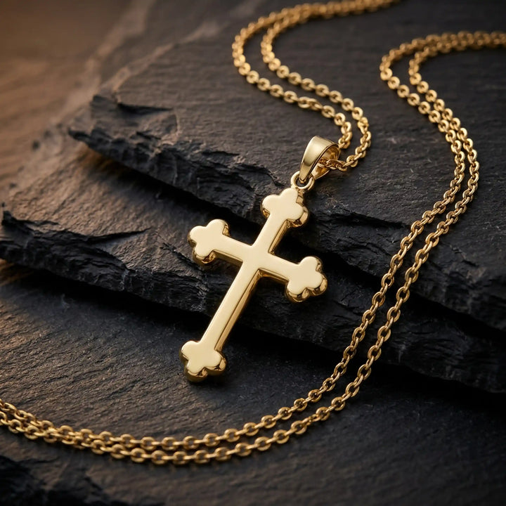 Cross fleury pendant necklace with fleur-shaped cross ends displayed on black stone.