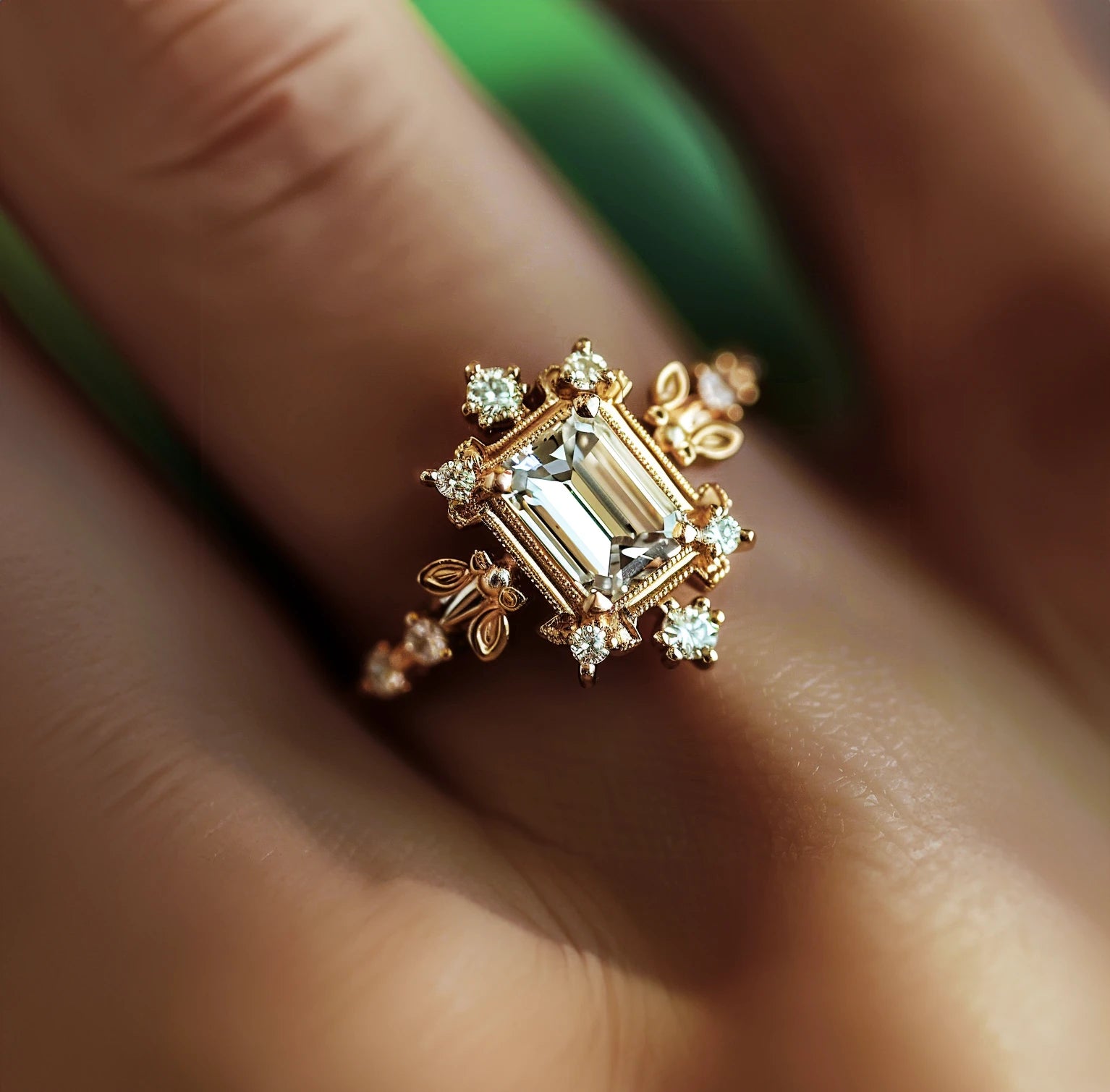A close-up of a vintage-style engagement ring with an emerald cut diamond surrounded by intricate floral designs and smaller diamonds, set in a rose gold band.