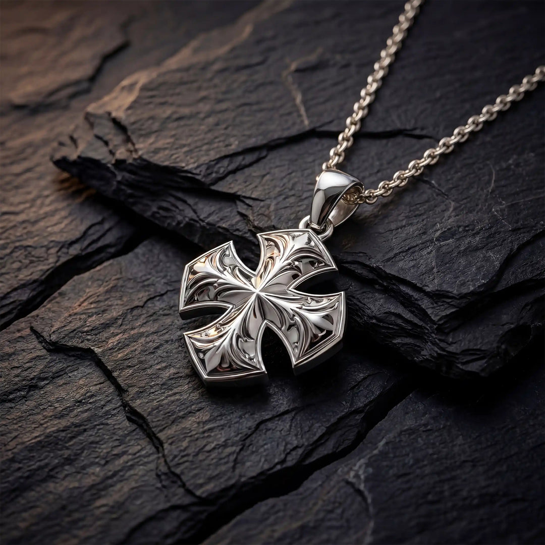 Maltese cross pendant with engraved ornamental design displayed on black stone.
