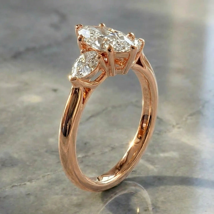 Marquise lab-grown diamond three-stone engagement ring with pear side stones on a polished surface.

