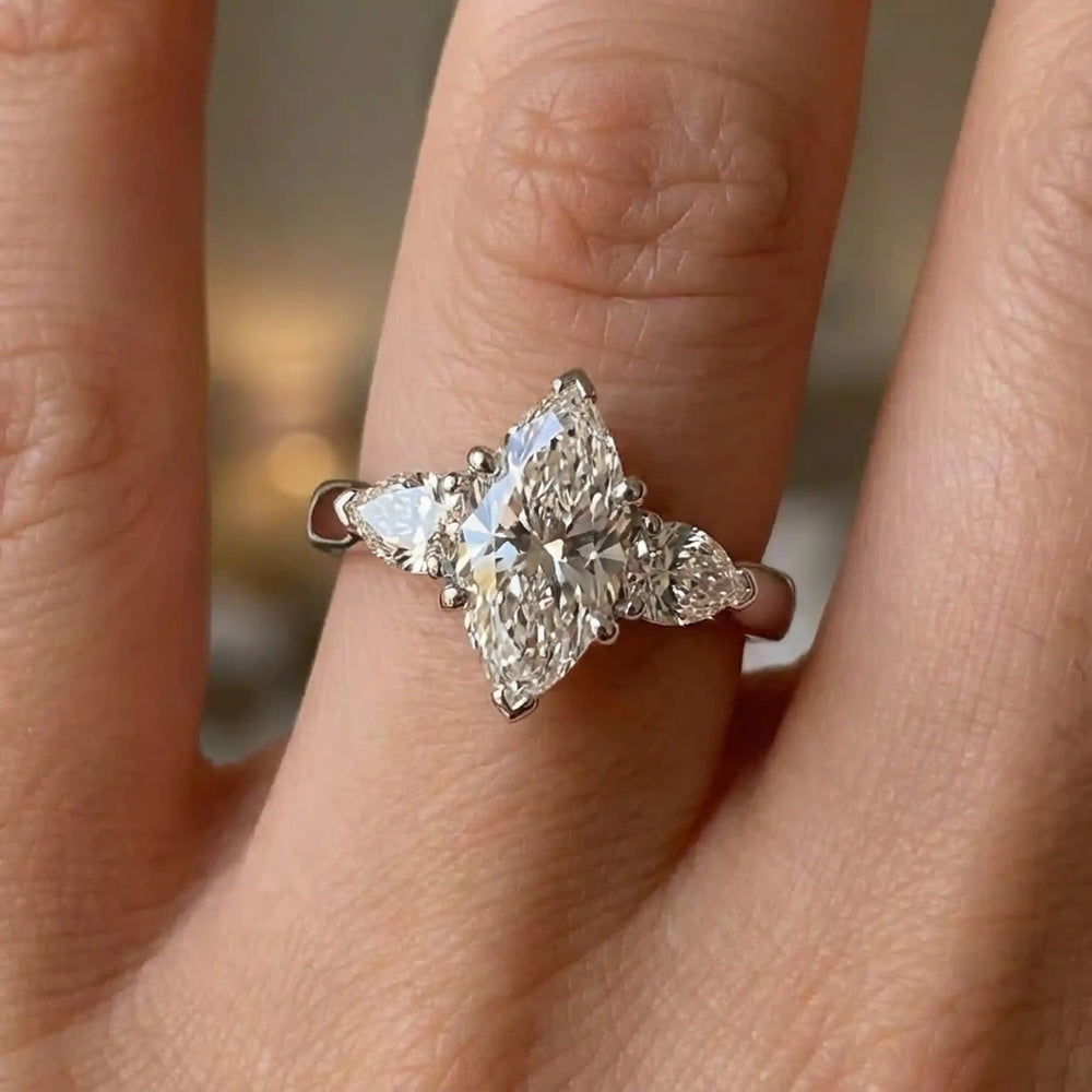 Marquise lab-grown diamond three-stone engagement ring with pear side stones on hand.

