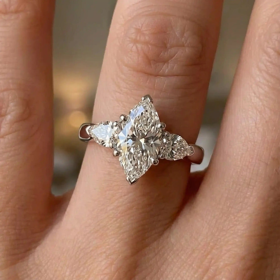 Marquise lab-grown diamond three-stone engagement ring with pear side stones on hand.
