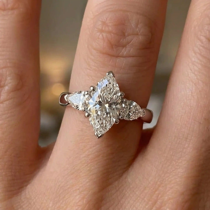 Marquise lab-grown diamond three-stone engagement ring with pear side stones on hand.
