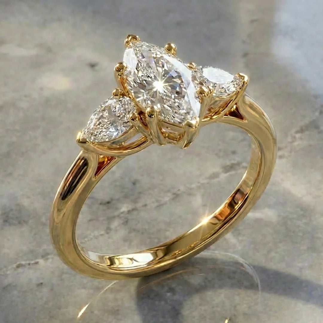 Marquise lab-grown diamond three-stone engagement ring with pear side stones on a polished surface.
