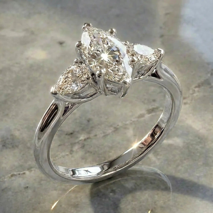 Marquise lab-grown diamond three-stone engagement ring with pear side stones on a polished surface.
