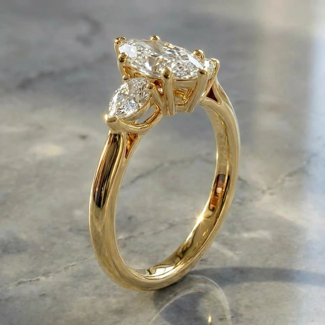 Marquise lab-grown diamond three-stone engagement ring with pear side stones on a polished surface.
