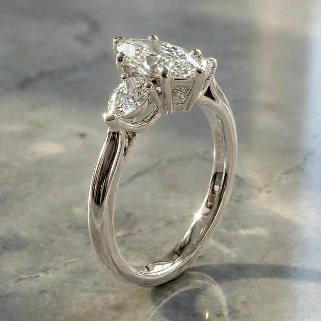 Marquise lab-grown diamond three-stone engagement ring with pear side stones on a polished surface.
