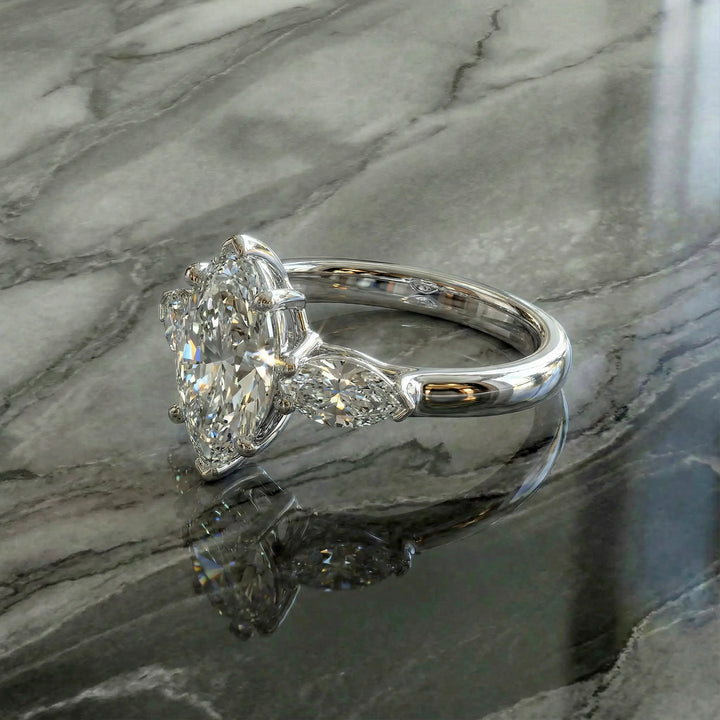 Marquise three-stone lab-grown diamond engagement ring shown on reflective surface.
