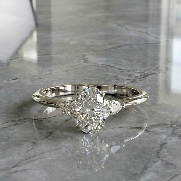 Oval diamond engagement ring with pear-shaped side stones front view.