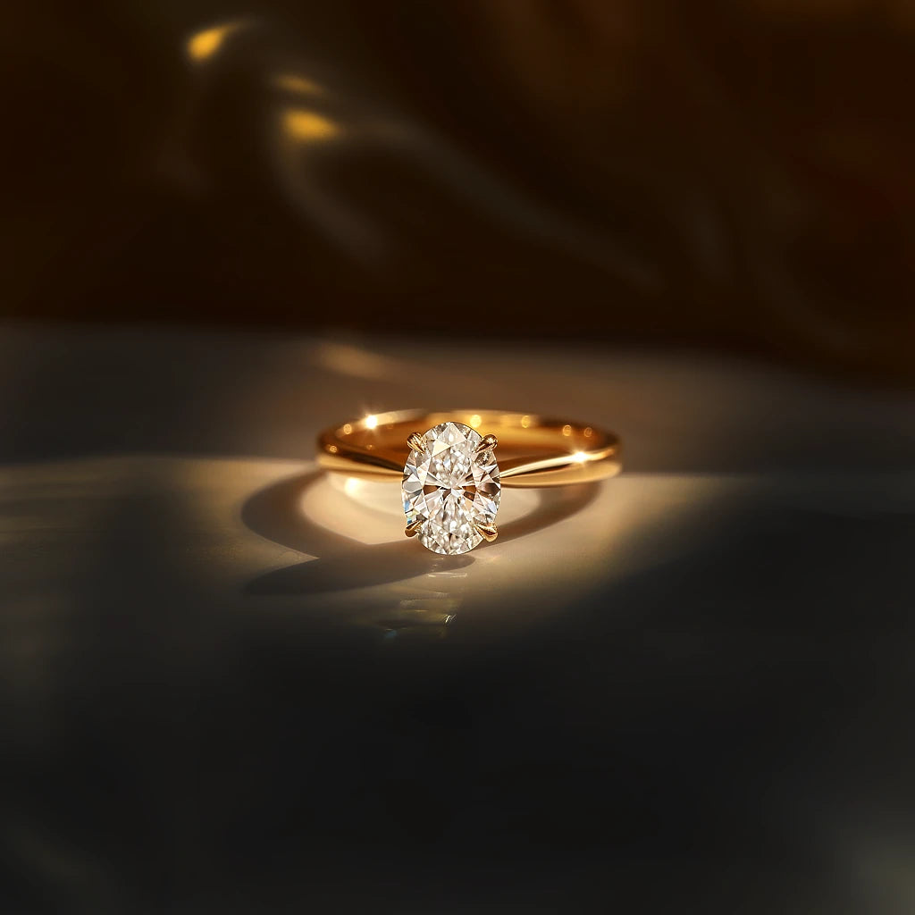 A close-up of an oval solitaire diamond ring set in a yellow gold band, beautifully lit against a soft background.